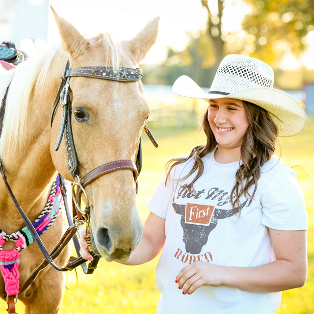 Ella Nipper standing next to her palomino horse, wearing a straw cowboy hat and smiling. 